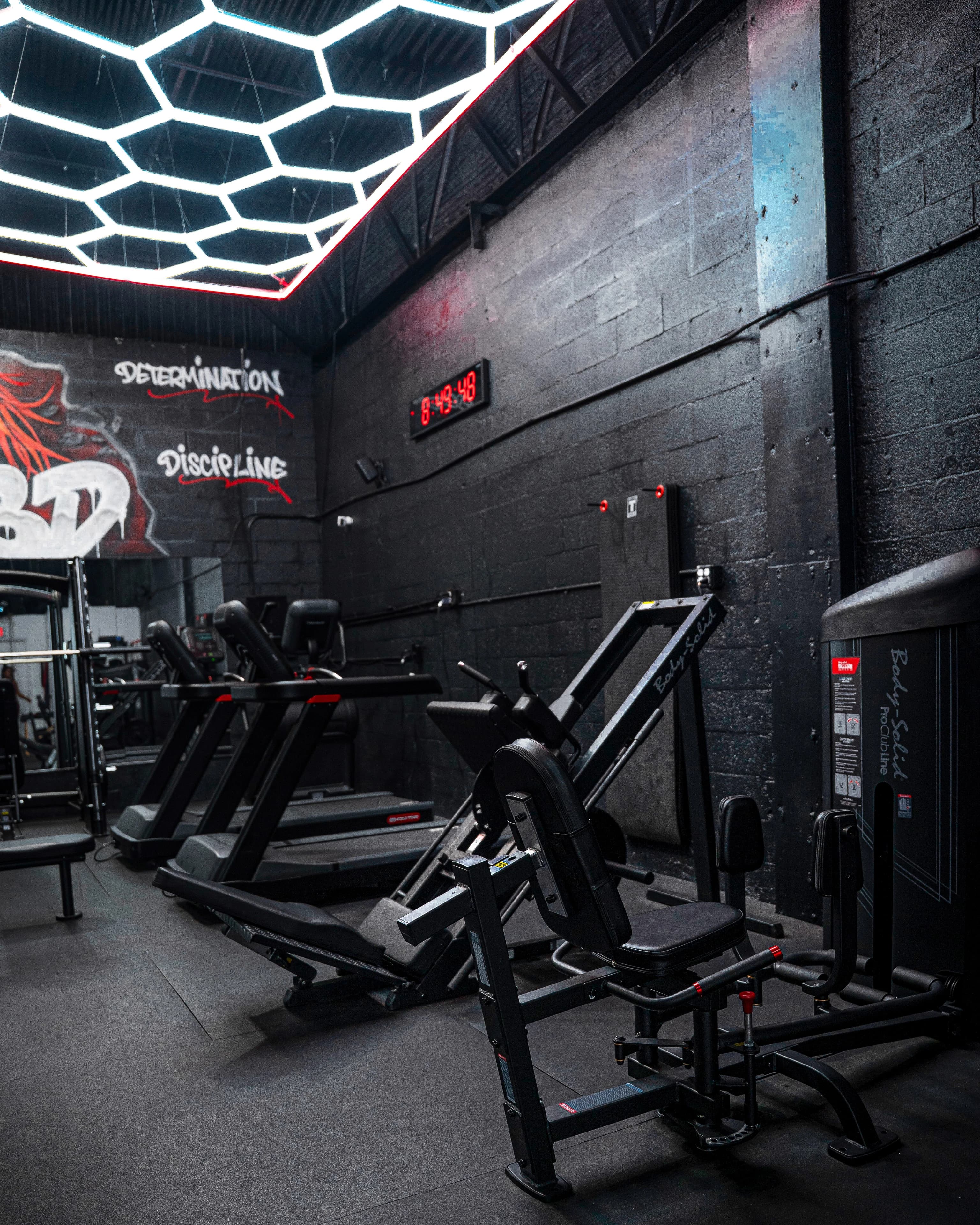Hexagon ceiling lights over treadmills and strength machines, with Determination and Discipline painted on the wall