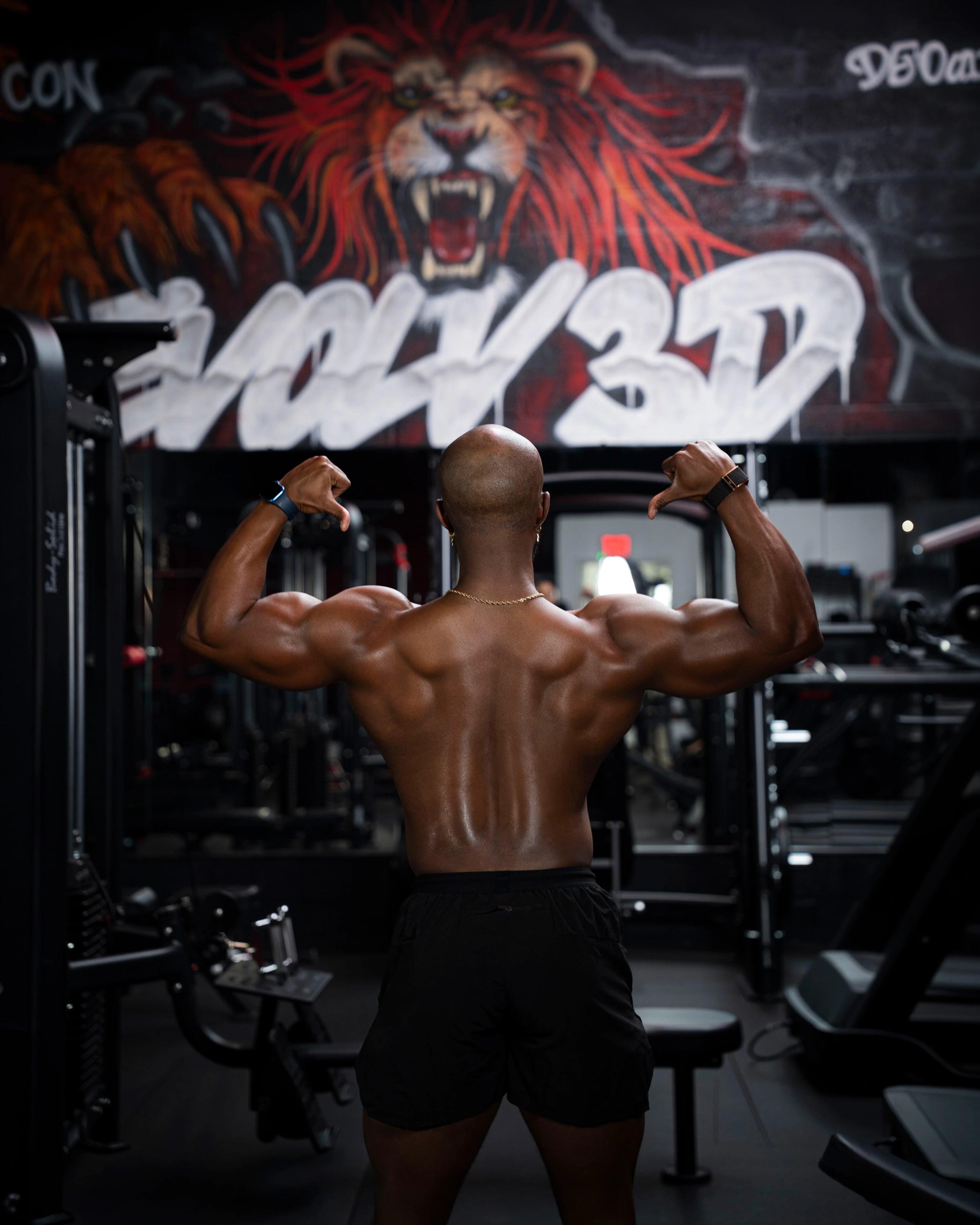 Daniel Triche flexing his back in front of the Evolv3D lion mural