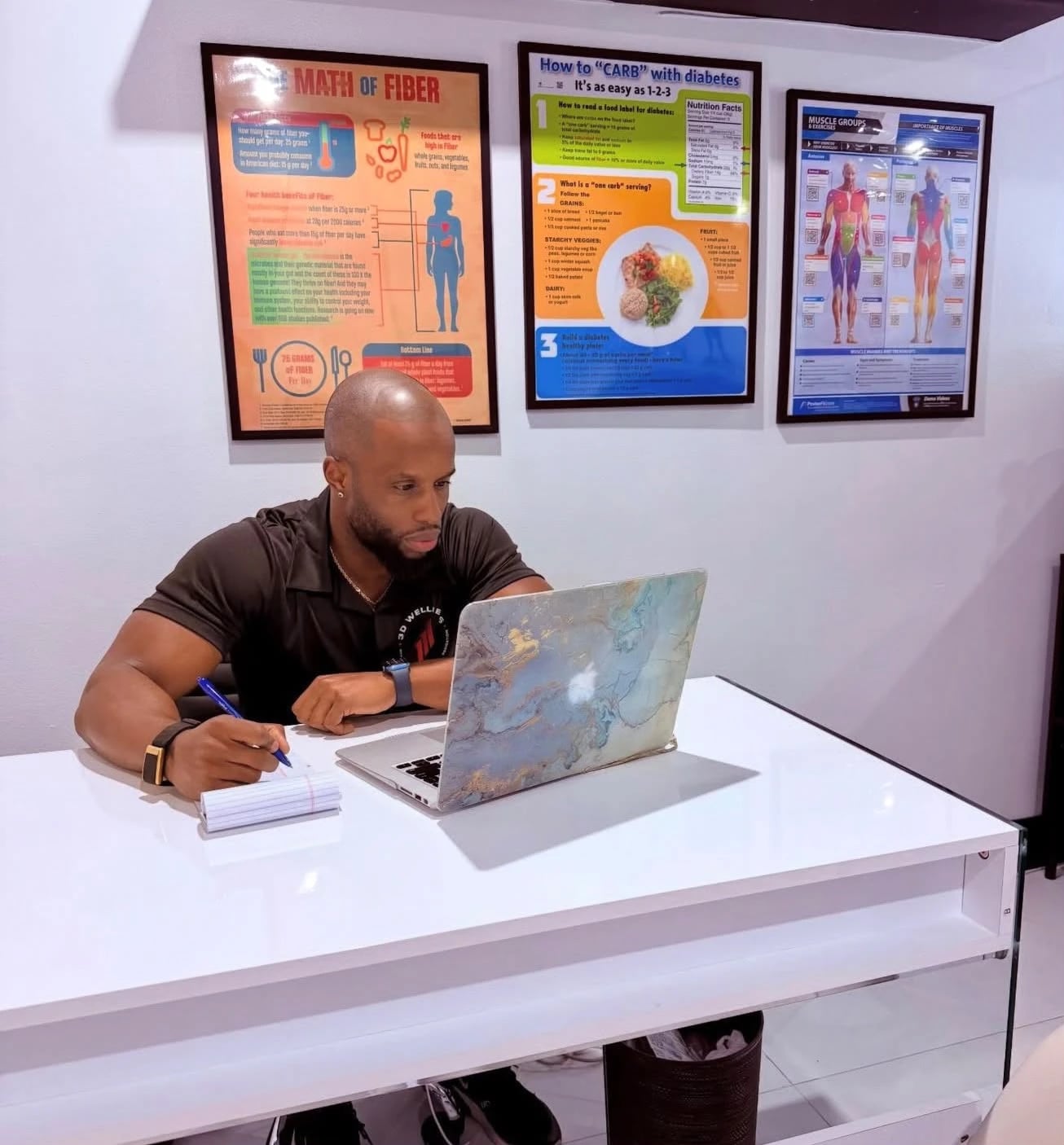 Daniel Triche working on a laptop at a desk beneath nutrition posters
